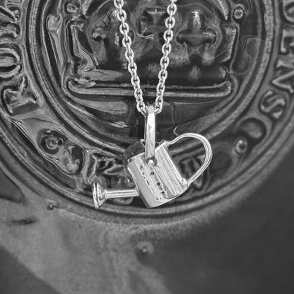 Watering can pendant made of silver draped over a plant pot