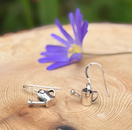 silver drop earrings with watering cans on, next to flowers