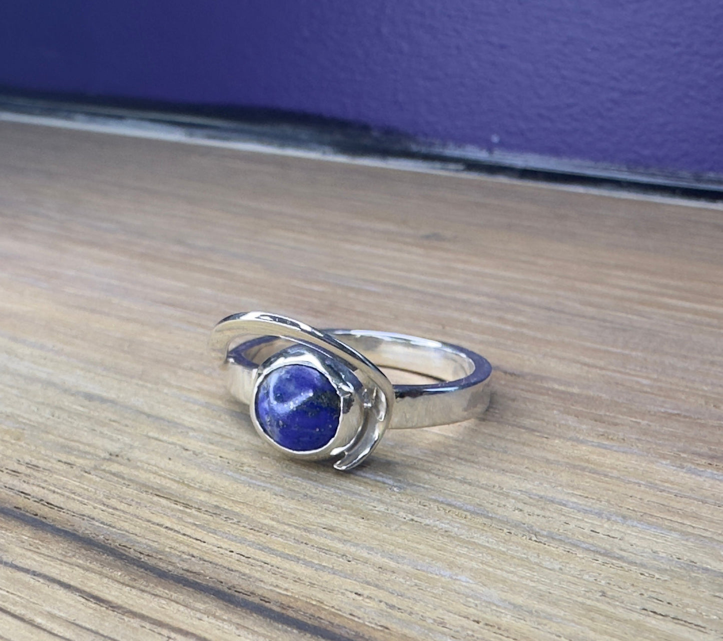 Silver ring with a blue stone on a wooden surface with a purple background