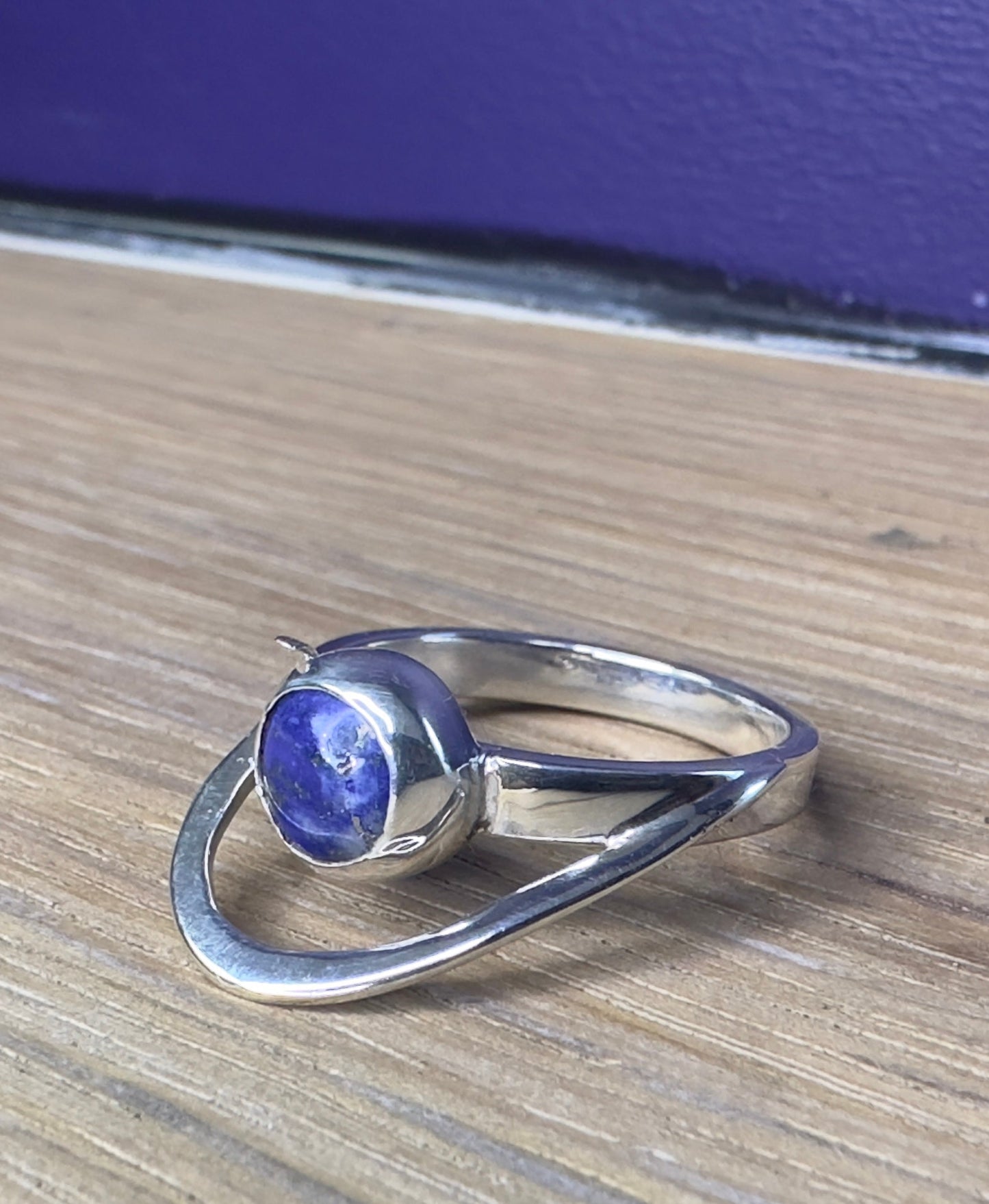Silver ring with a blue gemstone on a wooden surface with a blue background