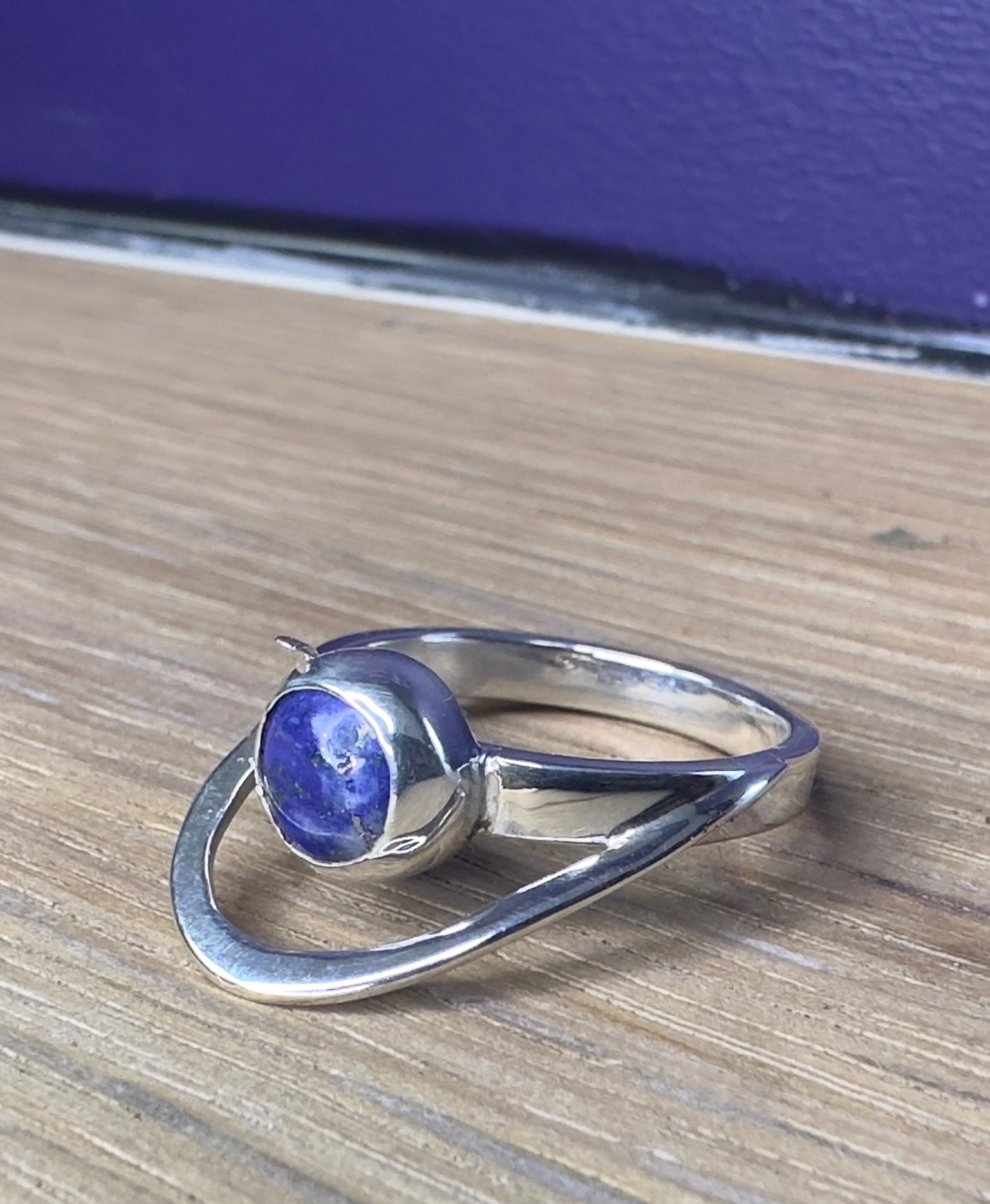 Silver ring with a blue gemstone on a wooden surface with a blue background